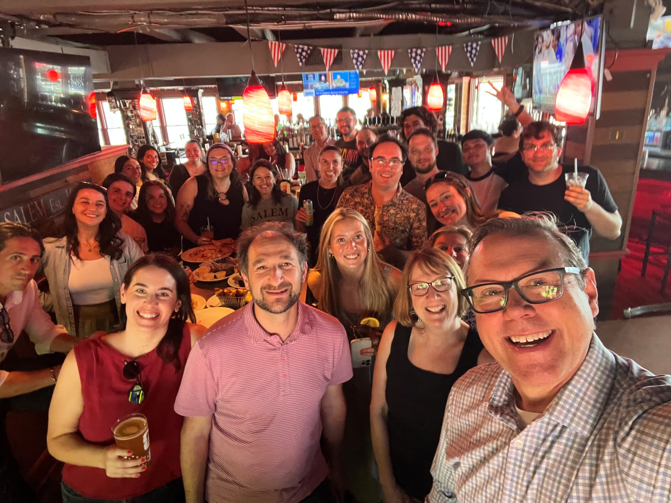 Arketi and Sperling Team Gathering A candid group selfie of the combined Arketi and Sperling team gathered inside a lively restaurant, with team members smiling around tables and standing together in an informal setting.
